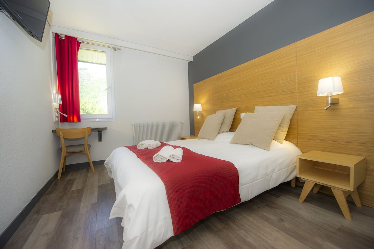 A hotel room with a bed, a chair, a nightstand, a lamp, and a window with curtains.