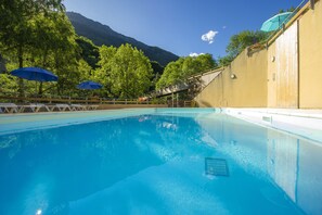 Una piscina con sillas de descanso y sombrillas, rodeada de árboles y montañas.