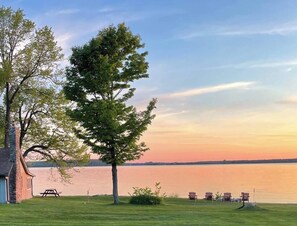 A lakeside view with a picnic table, chairs, and a stone building. - Thenell's Cottage - Rustic charm, steps from the Bay (Sturgeon Bay)