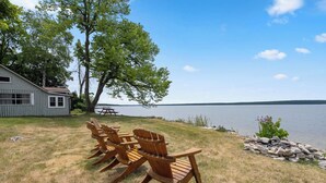 Une scène au bord d’un lac, avec une maison, des chaises en bois et une table de pique-nique.