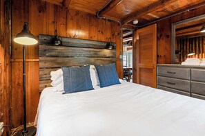 A wooden-paneled bedroom with a bed, a dresser, and a lamp.