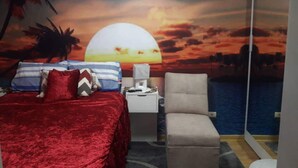 Camera da letto con un letto, una sedia, un comodino e un murale raffigurante un tramonto sull'acqua.