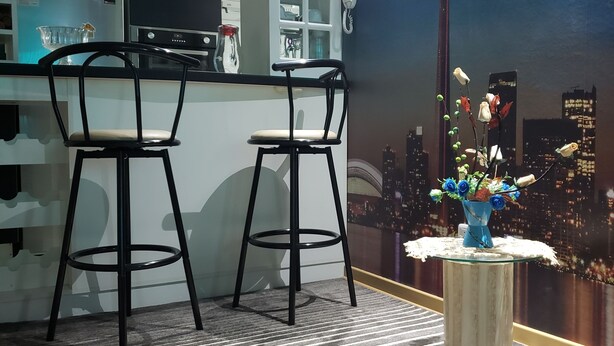 Una cucina moderna con due sgabelli da bar, un vaso decorativo con fiori e un murale raffigurante un panorama urbano.