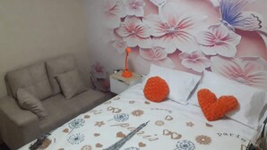 Una camera da letto con un letto, cuscini, un comodino e una parete decorata con motivi floreali e farfalle.