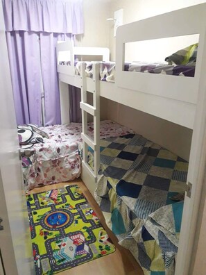 Cozy single-room accommodation with a bunk bed arrangement, a small bed, and a colorful rug.