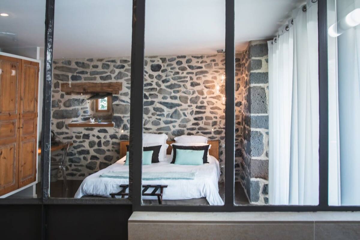 Une chambre avec un mur en pierre, un cadre de lit en bois et une fenêtre avec des rideaux.