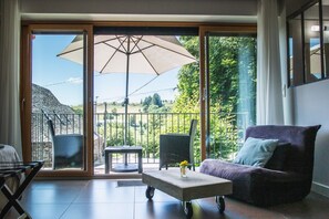 A modern living room with a sliding glass door leading to a balcony, a large umbrella, a purple sofa, and a small table with a vase. - Aux Caprices d'Aubrac (Laguiole)