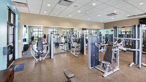 Un gimnasio con varias máquinas de ejercicio, un reloj en la pared y una puerta con un cartel.