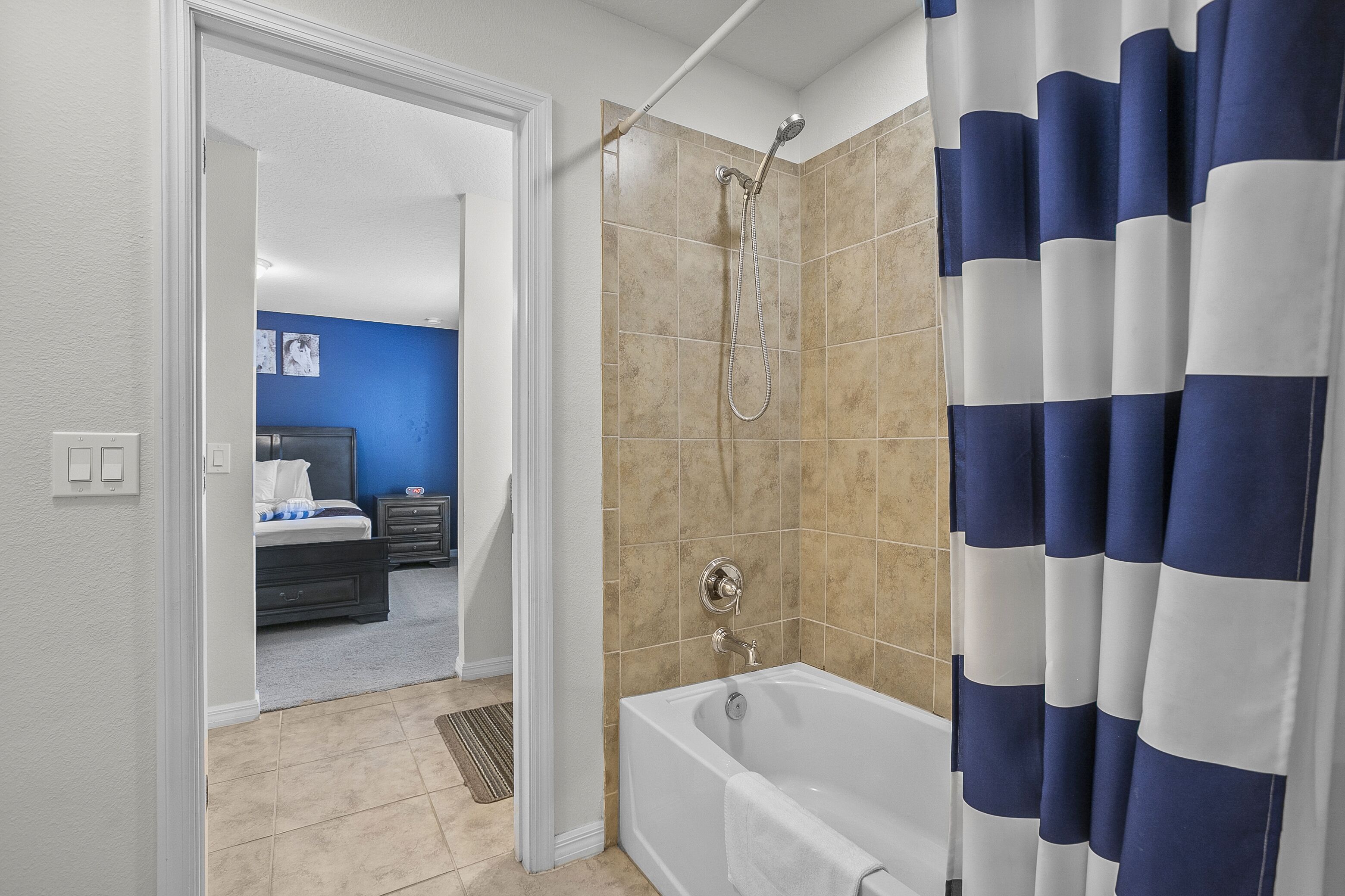 Un baño con bañera, ducha y cortina de ducha a rayas azules.