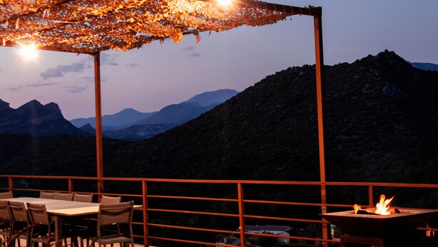 Un espacio al aire libre con mesa y sillas, un hogar para la fogata y vistas a las montañas.