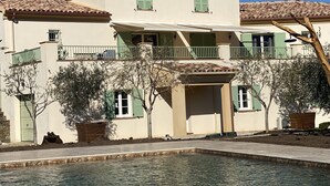 Un edificio de dos pisos con techo de tejas, contraventanas verdes y una zona de piscina.