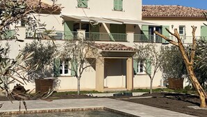 Un edificio de dos pisos con piscina, rodeado de olivos y un cielo azul despejado.