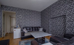 Cozy living space with a sofa, armchair, kitchenette, and dining table, perfect for short stays or work.