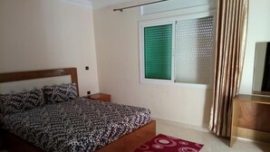 Ein Schlafzimmer mit einem Bett, einem Nachttisch, einem Fenster mit Jalousien und einem Vorhang.