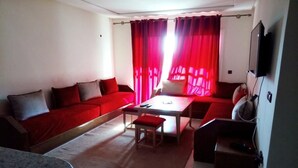 Ein Wohnzimmer mit einem roten Sofa, einem kleinen Tisch und einem an der Wand befestigten Fernseher.