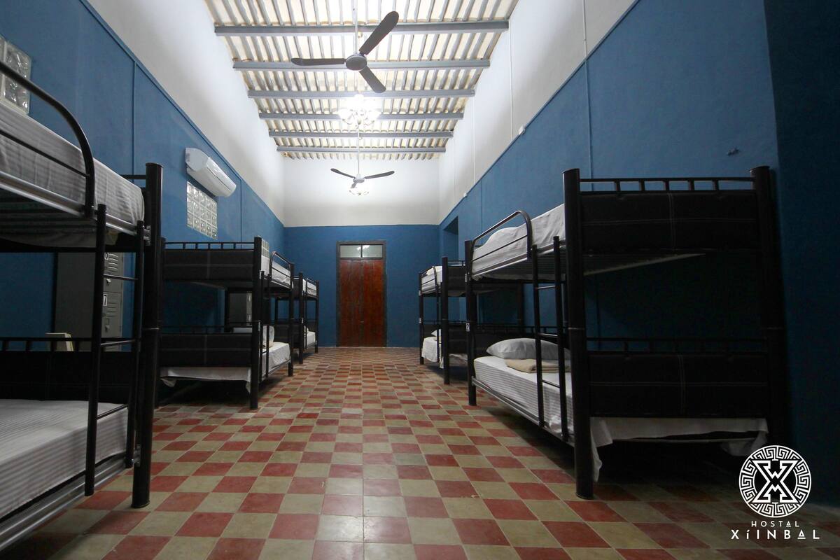 A hostel room with bunk beds, a checkered floor, and a ceiling fan.