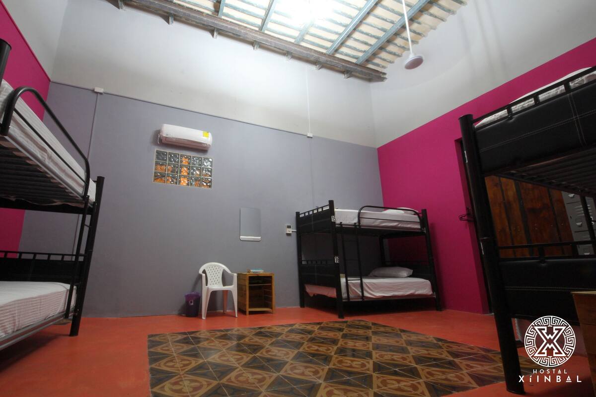 A hostel room with bunk beds, a small white chair, a tiled floor, and a window with a view.