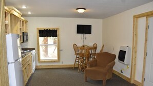 Een compacte kamer met een kitchenette, een eettafel met stoelen, een bruine fauteuil, een flatscreen-tv aan de muur en een verwarming op de vloer.