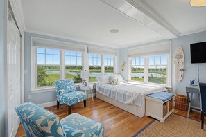A bedroom with a large window overlooking a natural landscape, a bed with a view, a chair, and a desk area.