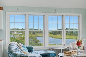 A room with a large window overlooking a lake, a blue sofa, and a small table with a vase.