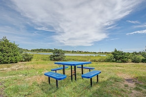 A picnic table with benches in a grassy field with a lake and trees in the background. - Views! Four bedroom sleeping 8 with views of West Dennis Beach (West Dennis)