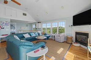 Amplia sala de estar con un sofá seccional azul grande, una chimenea y ventanas amplias que ofrecen vistas al exterior.