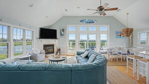 Amplia sala de estar con un sofá azul grande, chimenea, televisor y comedor con mobiliario blanco.