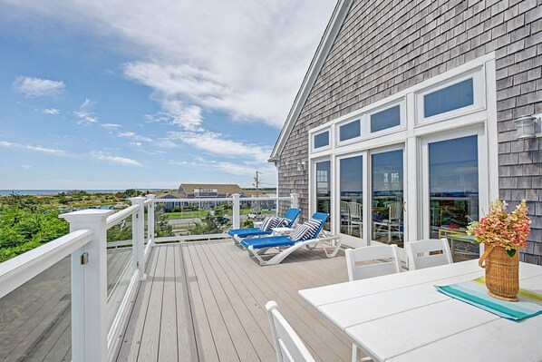 A deck with lounge chairs and a table, overlooking a beach and ocean.