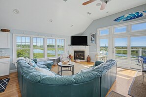 A spacious living room with a curved sofa, a fireplace, and large windows offering a view of the outdoors.