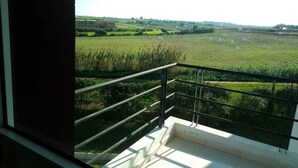A balcony with a view of a green field and distant buildings.