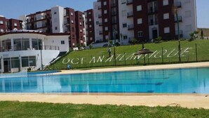 A swimming pool with a grassy area in front, surrounded by multi-story residential buildings.