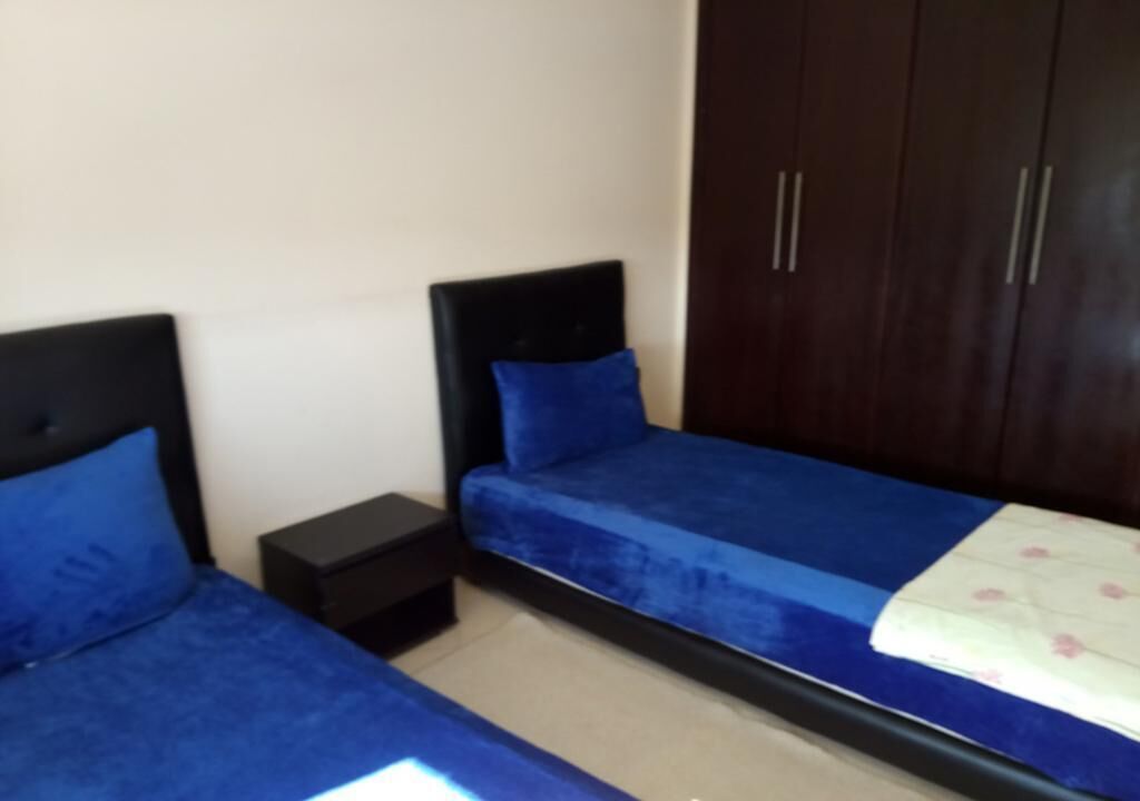 A bedroom with two single beds, a dark wooden wardrobe, and a small bedside table.