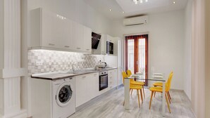 A compact kitchen with a washing machine, a microwave, and a dining area with yellow chairs. - Stylish 2 Bedroom Apartment in an Amazing Location (Sliema)