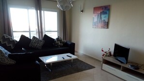 Un salon avec un canapé, une table basse, un téléviseur posé sur un meuble et un tableau accroché au mur.