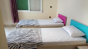 Deux lits simples avec des couvertures à motifs zébrés, une tête de lit de couleur turquoise et une fenêtre avec des stores.