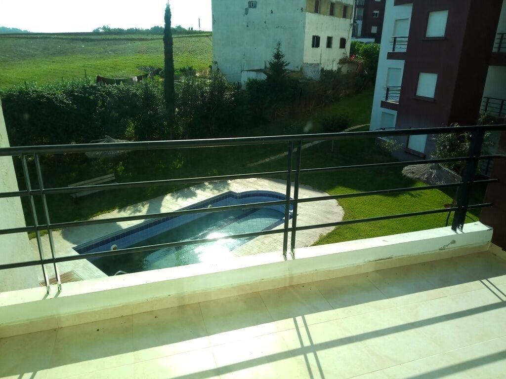 Un balcon donnant sur une piscine, une pelouse et un bâtiment situé au loin.