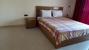 Une chambre à coucher avec un lit en bois, une table de chevet dotée de tiroirs et un rideau rouge.