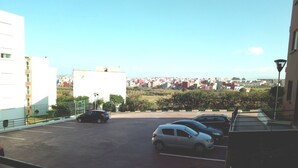 Un espace de stationnement avec plusieurs voitures, une vue sur un paysage urbain en arrière-plan et un bâtiment avec un balcon sur la droite.