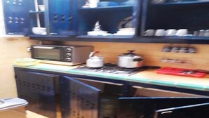 Una cocina con microondas, estufa y diversos utensilios de cocina. Hay armarios sobre la encimera y un cubo de basura a la izquierda.