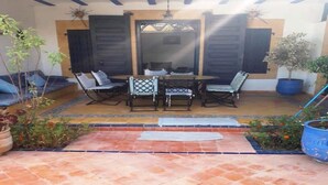 Un patio al aire libre con una mesa y sillas, rodeado de macetas con plantas y un piso de baldosas.