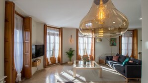 Ein modernes Wohnzimmer mit großem Fernseher, einer Couch, einem Couchtisch und einer Pendelleuchte.