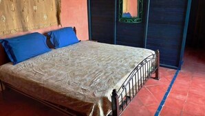 Ein Bett mit einem gemusterten Überwurf, einem blauen Kissen und einem Metall-Kopfstück.