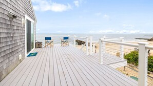 Eine Holzterrasse mit zwei blauen Stühlen, einem weißen Geländer und Blick auf das Meer.
