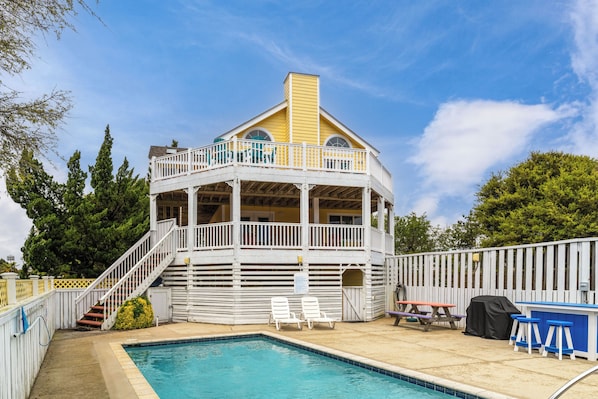 A two-story building with a pool, a covered patio area, and a barbecue setup.