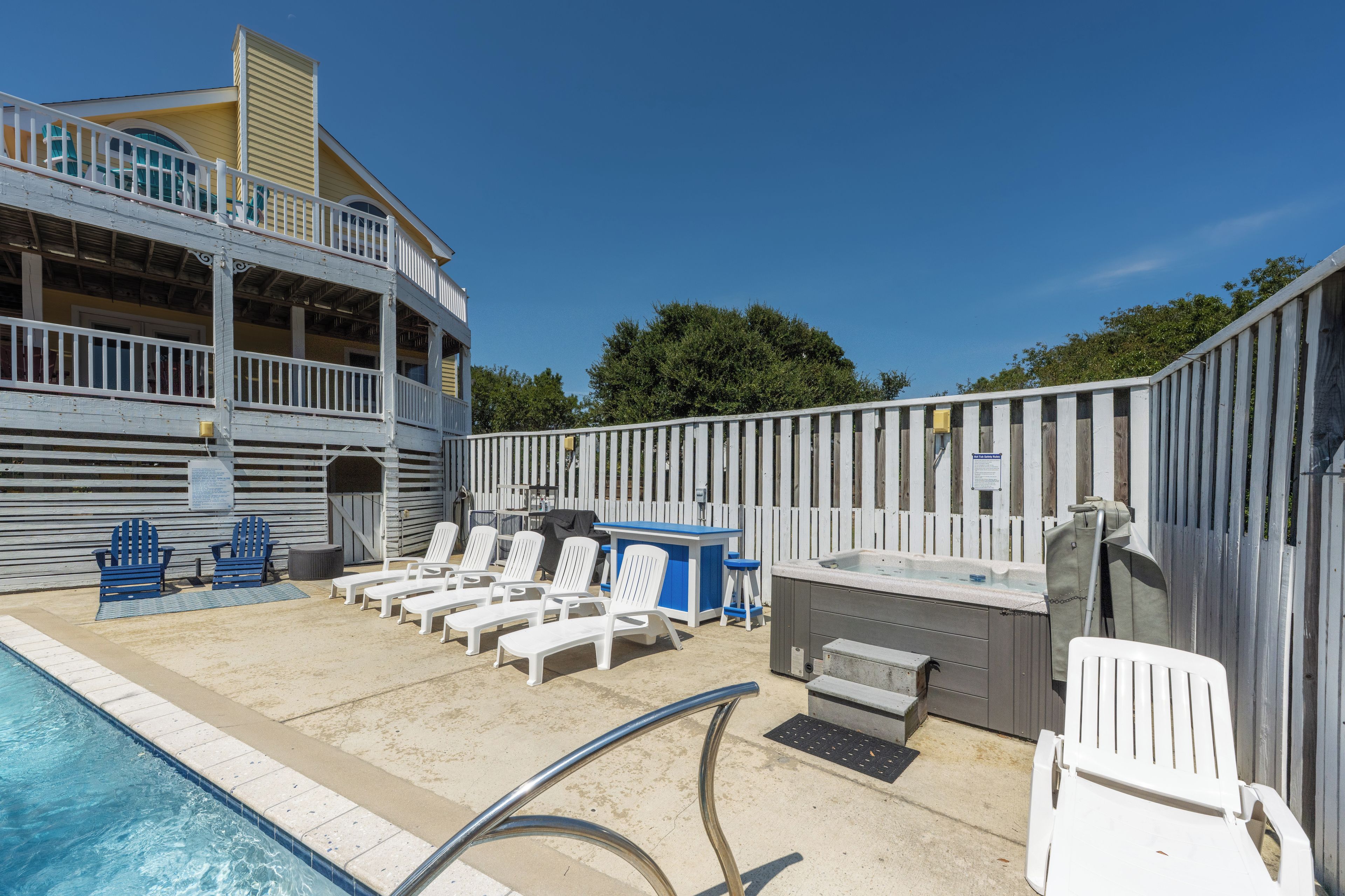 A pool area with lounge chairs, a hot tub, and a building with a balcony.