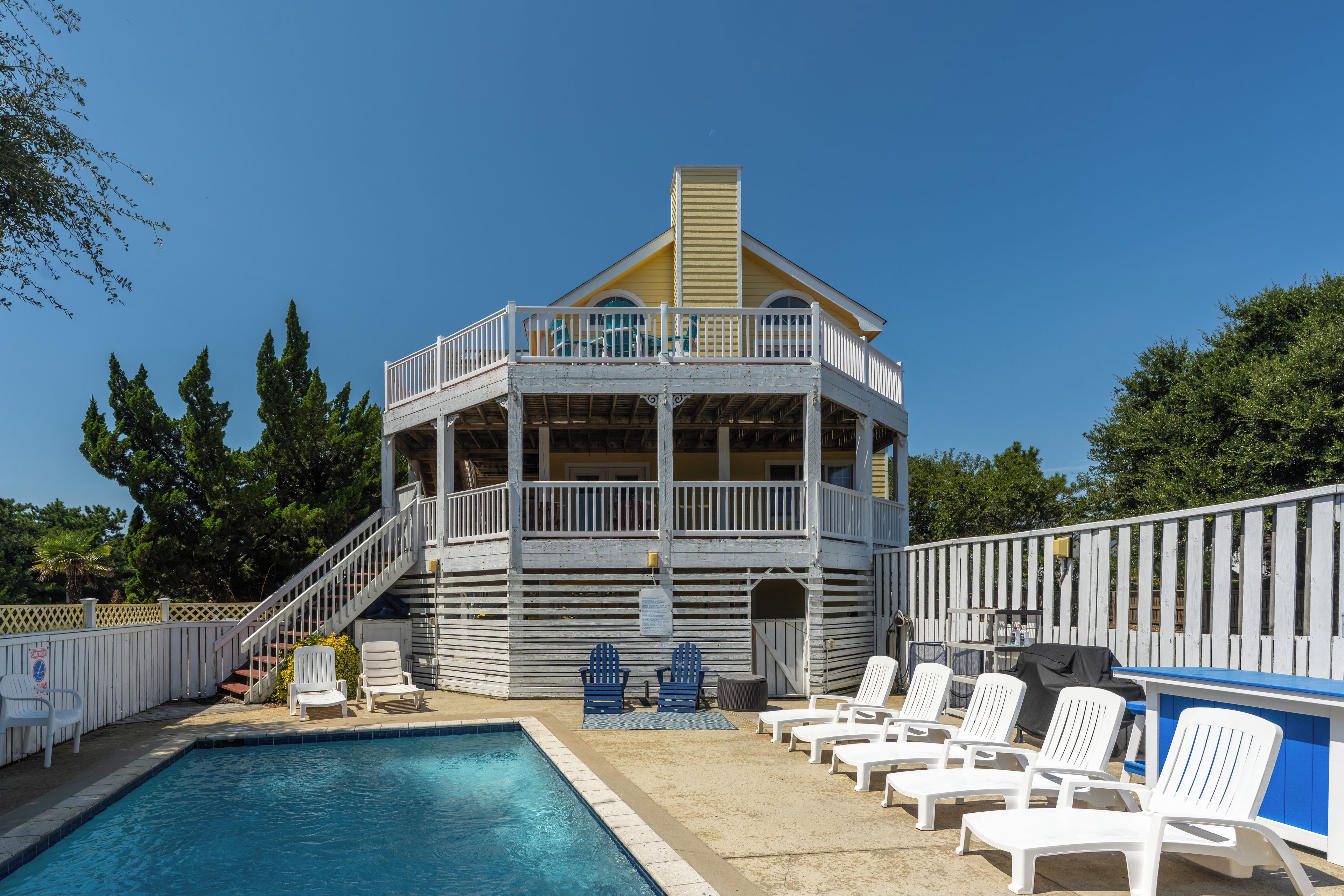 A pool area with a building that has a balcony and a staircase leading to it. There are lounge chairs and a pool.
