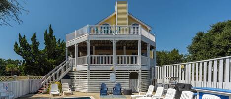 A pool area with a building that has a balcony and a staircase leading to it. There are lounge chairs and a pool.