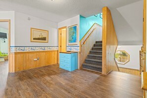 A spacious hallway with wooden flooring, a blue cabinet, and a staircase with wooden railings.