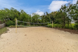 A sandy volleyball court with a net, surrounded by trees and a wooden fence.