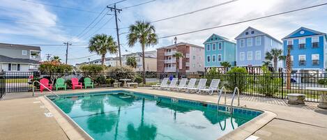 A rectangular pool with a clear blue water surface, surrounded by a concrete deck. There are lounge chairs and a small table near the pool, and a fence enclosing the area.